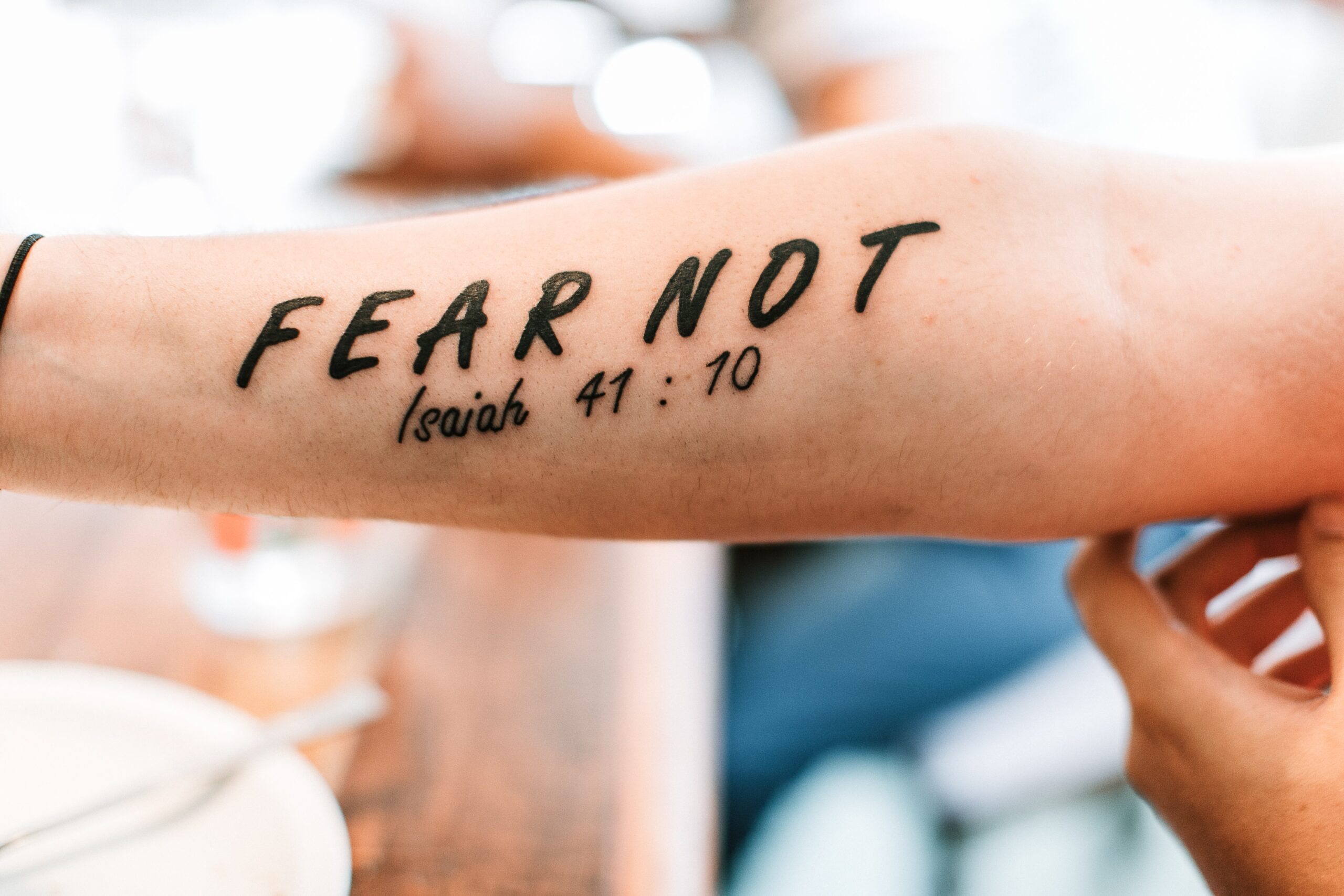 Inner arm tattoo of the words "Fear Not" with the verse Isaiah 41:10